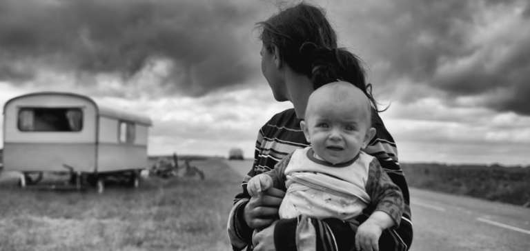 Zwart wit foto van vrouw met baby in de hand en een caravan op de achtergrond